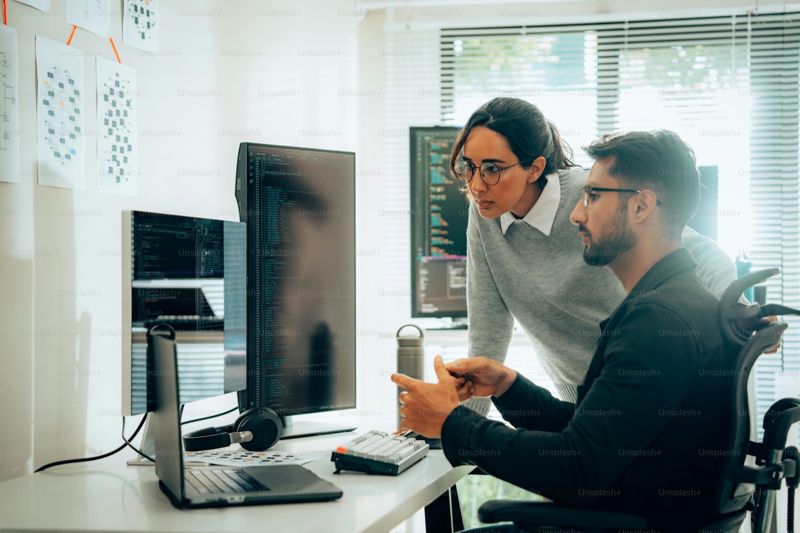 Two developers pairing at a bright office desk, reviewing code on a laptop together